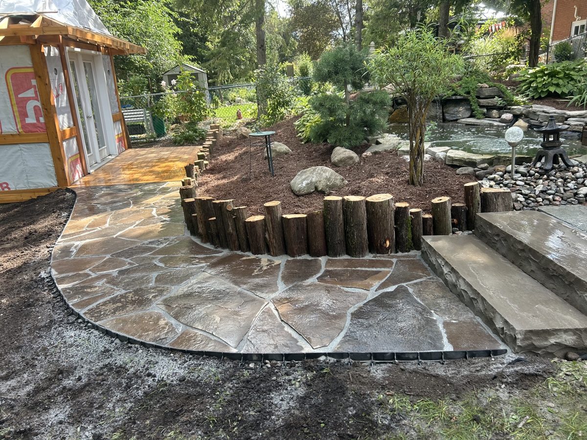 Flagstone path curving past a cedar-stump retaining wall and freshly mulched garden bed, Peterborough