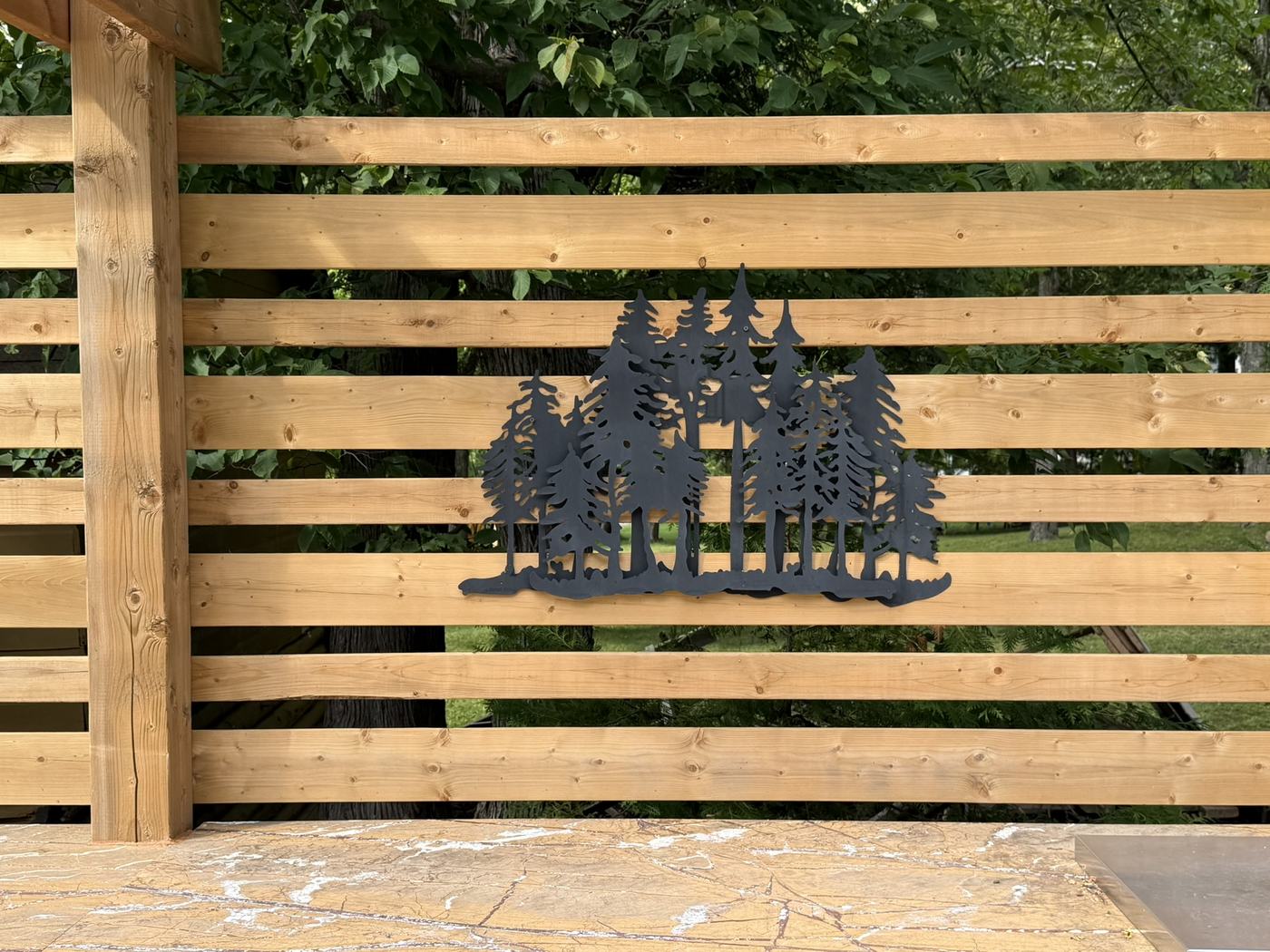 Cedar slat privacy screen with metal tree silhouette art backing an outdoor kitchen, Lakefield
