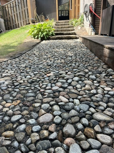 River-rock pathway with edging installed alongside a wood deck, Peterborough